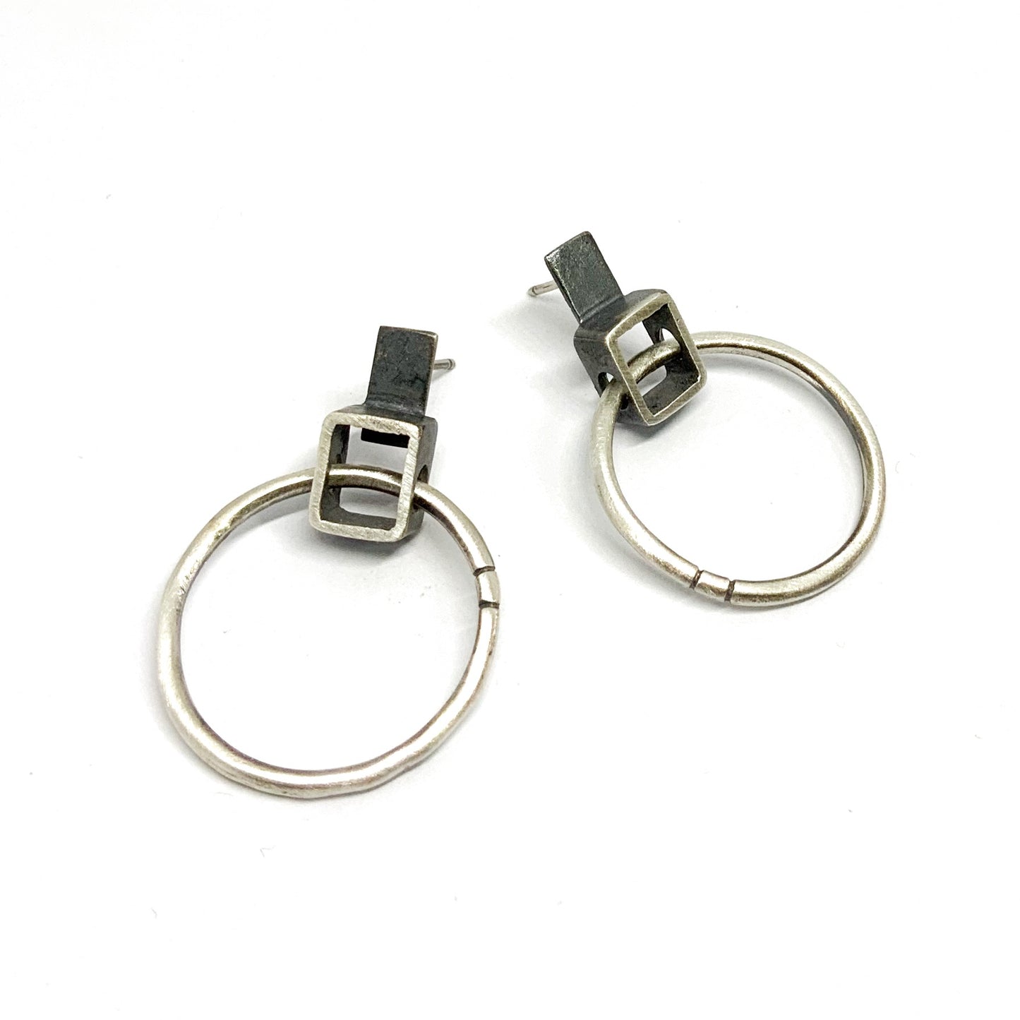 A pair of silver oxidized and brushed finish earrings with a geometric design, displayed against a white background.