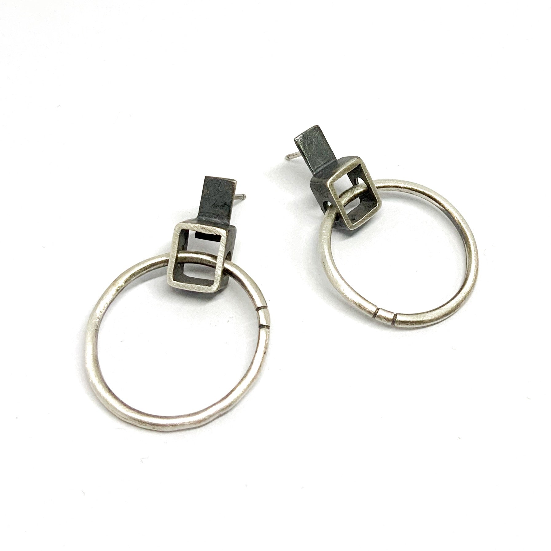 A pair of silver oxidized and brushed finish earrings with a geometric design, displayed against a white background.