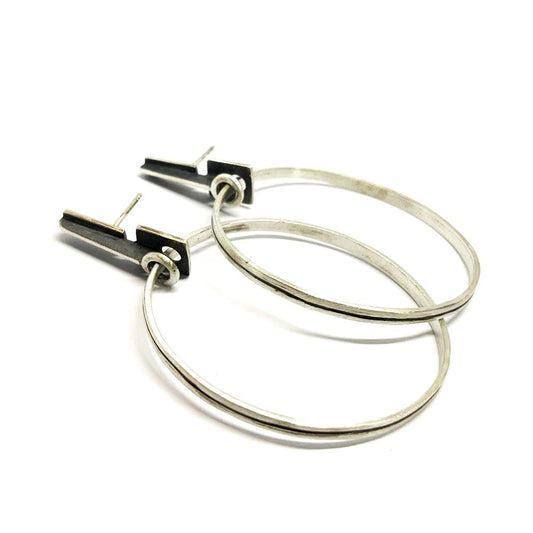 A pair of silver oxidized and brushed finish earrings with a geometric design, displayed against a white background.