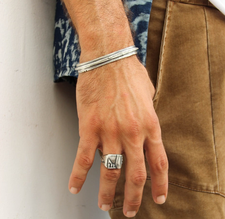 A sterling silver bracelet with an oxidized and brushed finish, featuring text on the bracelet surface.