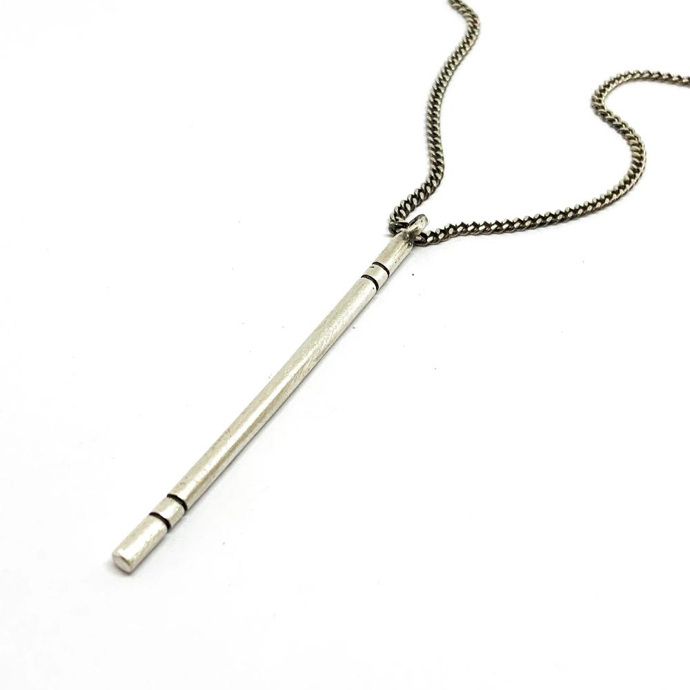 A silver necklace with a pendant resembling a walking stick, on a white background.