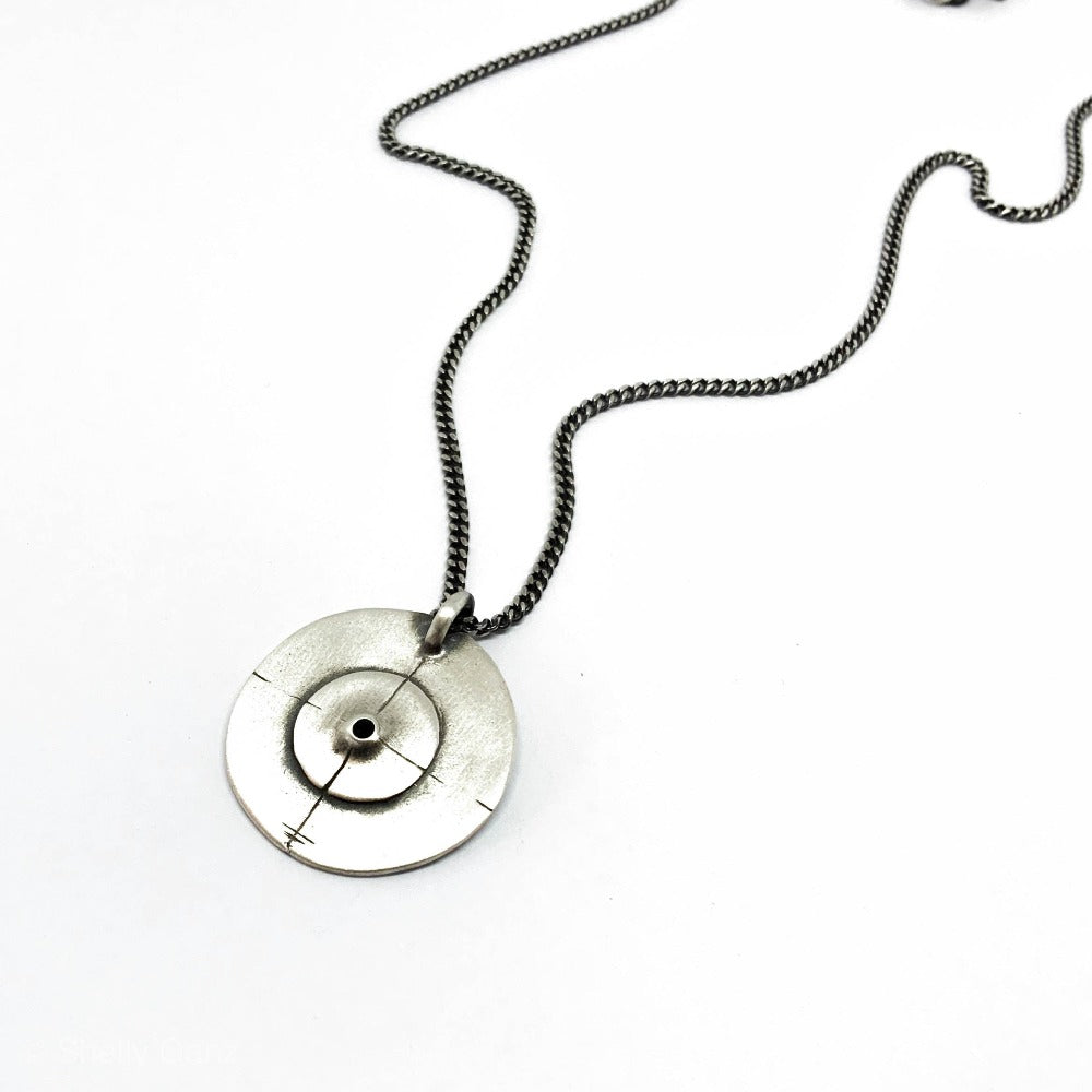 A silver necklace with a pendant featuring a circular design and a chain that ends in a pendant loop.