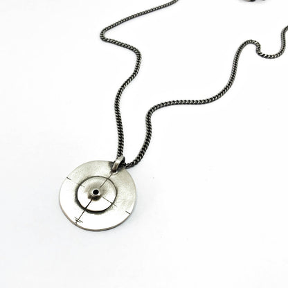 A silver necklace with a pendant featuring a circular design and a chain that ends in a pendant loop.