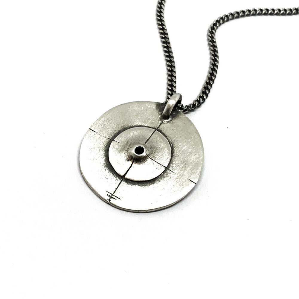 A silver necklace with a pendant featuring a circular design and a chain that ends in a pendant loop.