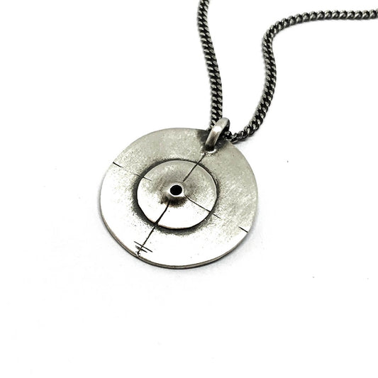 A silver necklace with a pendant featuring a circular design and a chain that ends in a pendant loop.