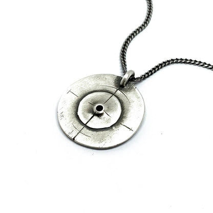 A silver necklace with a pendant featuring a circular design and a chain that ends in a pendant loop.