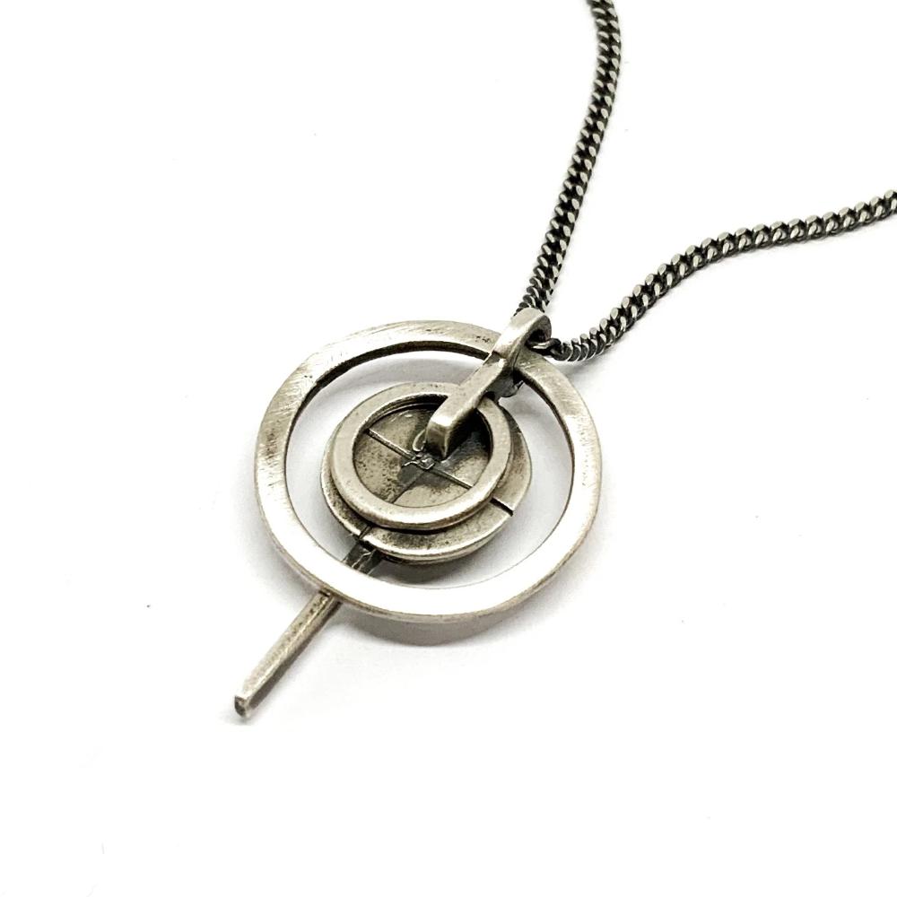A silver necklace with a pendant featuring a circular design and a chain that ends in a pendant loop.