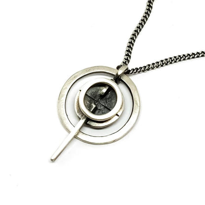 A silver necklace with a pendant featuring a circular design and a chain that ends in a pendant loop.