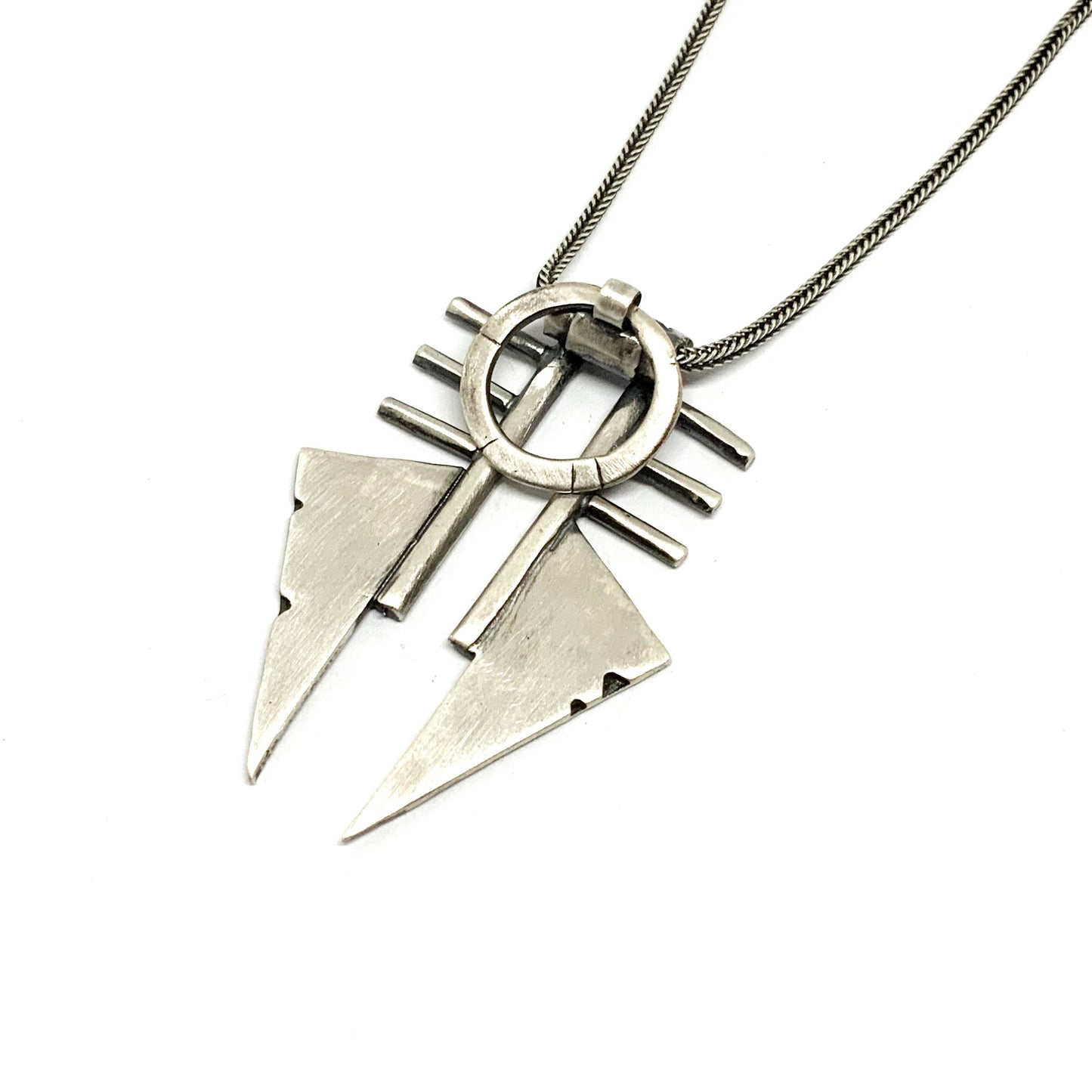 A sterling silver necklace with a pendant featuring two triangles and a circular ornament, with a brushed and oxidized finish.
