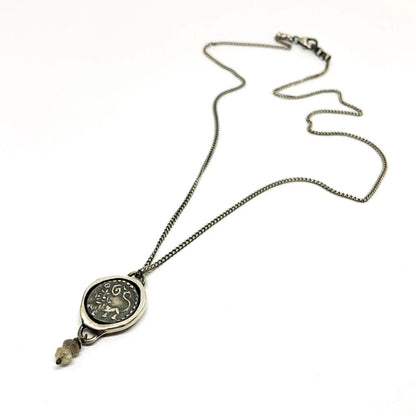 A silver necklace with a pendant featuring an ancient Hindu coin design with the figure of Hanuman- Monkey god, accompanied by two tiny labradorite stones.