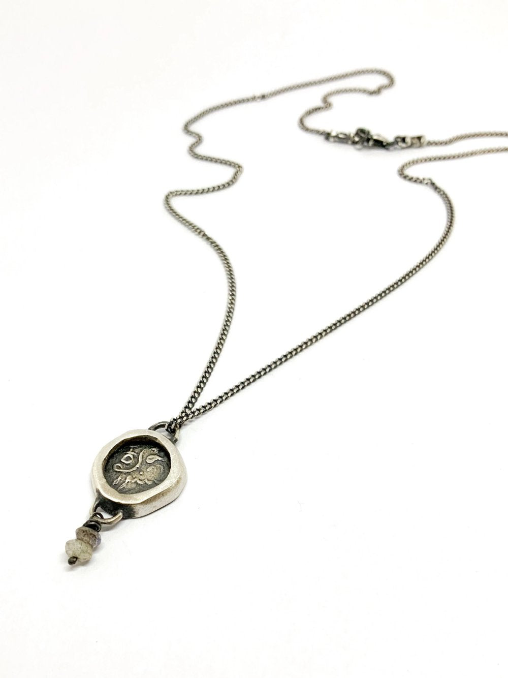 A silver necklace with a pendant featuring an ancient Hindu coin design with the figure of Hanuman- Monkey god, accompanied by two tiny labradorite stones.