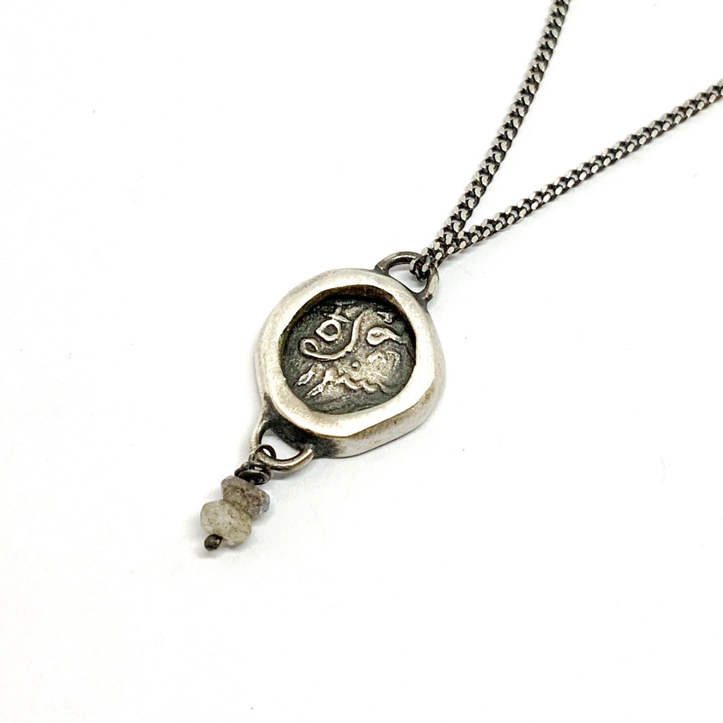 A silver necklace with a pendant featuring an ancient Hindu coin design with the figure of Hanuman- Monkey god, accompanied by two tiny labradorite stones.
