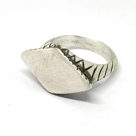A silver ring with an oxidized and brushed finish, featuring a textured design on the top part.