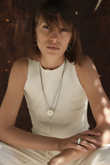 A silver necklace with a pendant featuring a circular design and a chain that ends in a pendant loop.