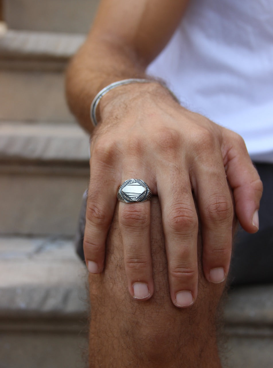 A silver signet ring with a geometric pattern on the top part, surrounded by a plain band.