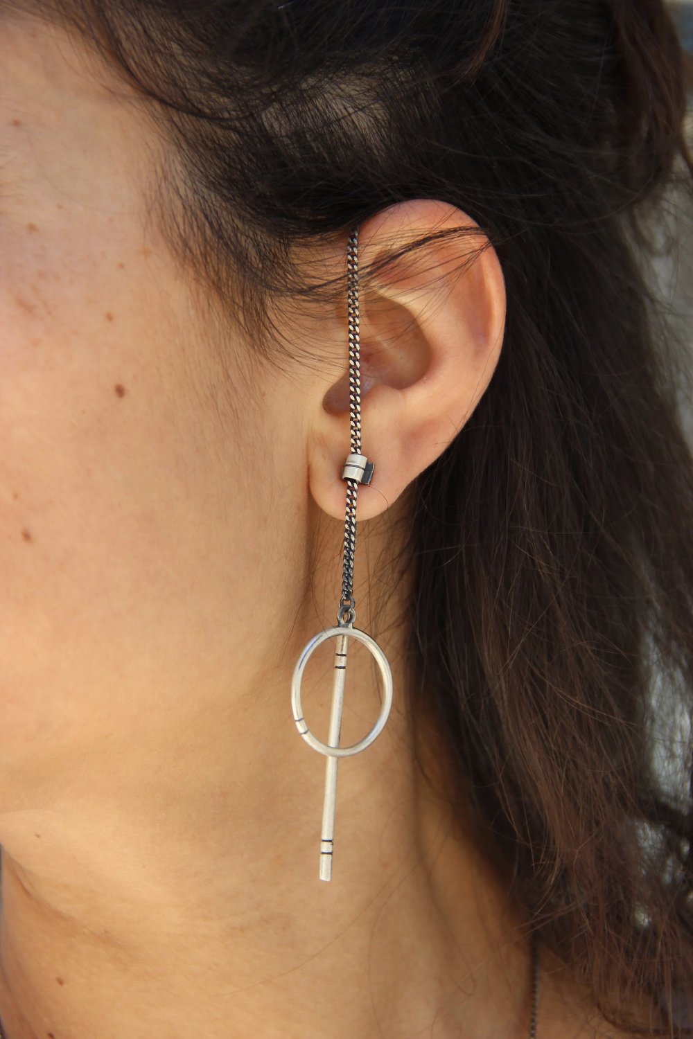 A pair of silver hoop earrings, one with a dangling tube design and the other with a chain hoop design, both made of sterling silver with a brushed finish.