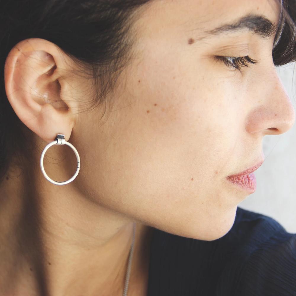 A pair of silver hoop earrings, one with a dangling tube design and the other with a chain hoop design, both made of sterling silver with a brushed finish.