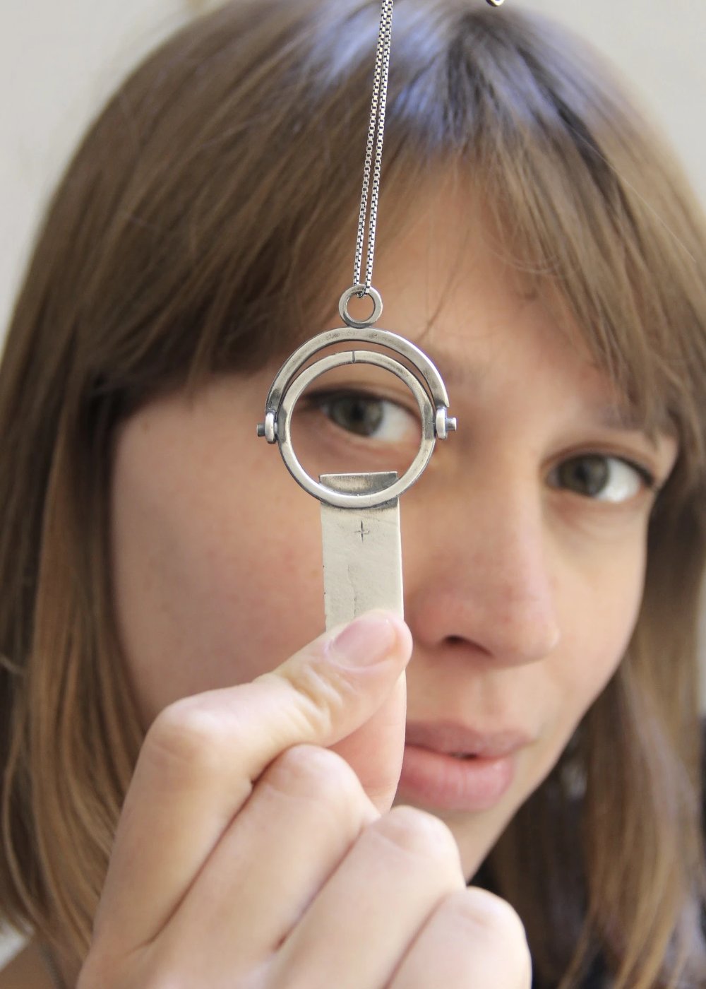 A sterling silver necklace with a magnifying glass pendant and a cross on the chain.
