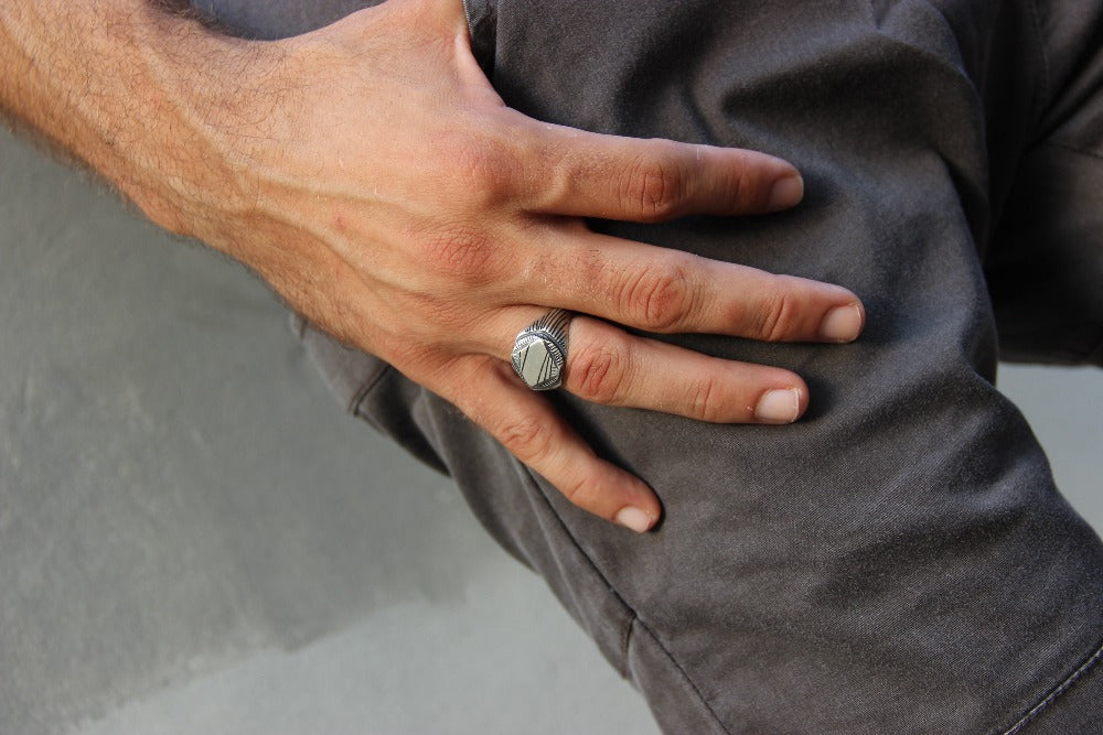 A silver signet ring with a geometric pattern on the top part, surrounded by a plain band.