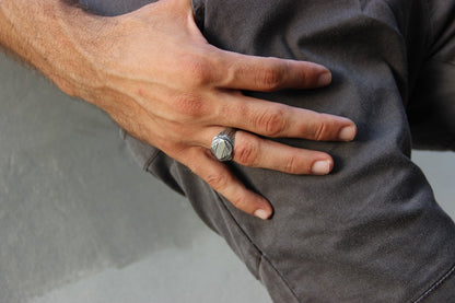A silver signet ring with a geometric pattern on the top part, surrounded by a plain band.