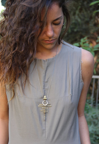 A silver-colored necklace with a pendant featuring a series of parallel lines and a circular ring