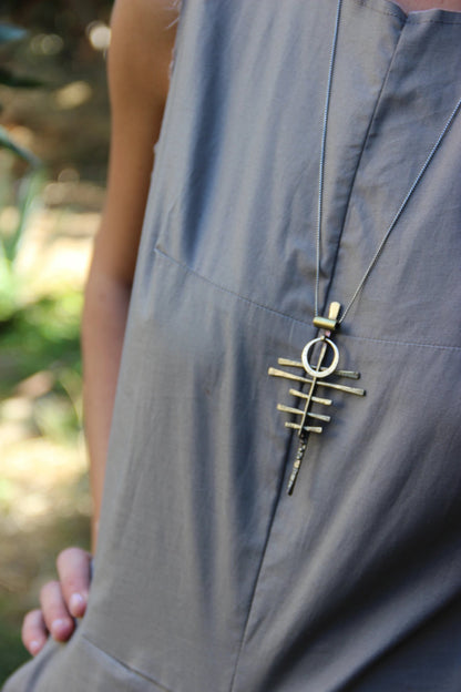 A silver-colored necklace with a pendant featuring a series of parallel lines and a circular ring