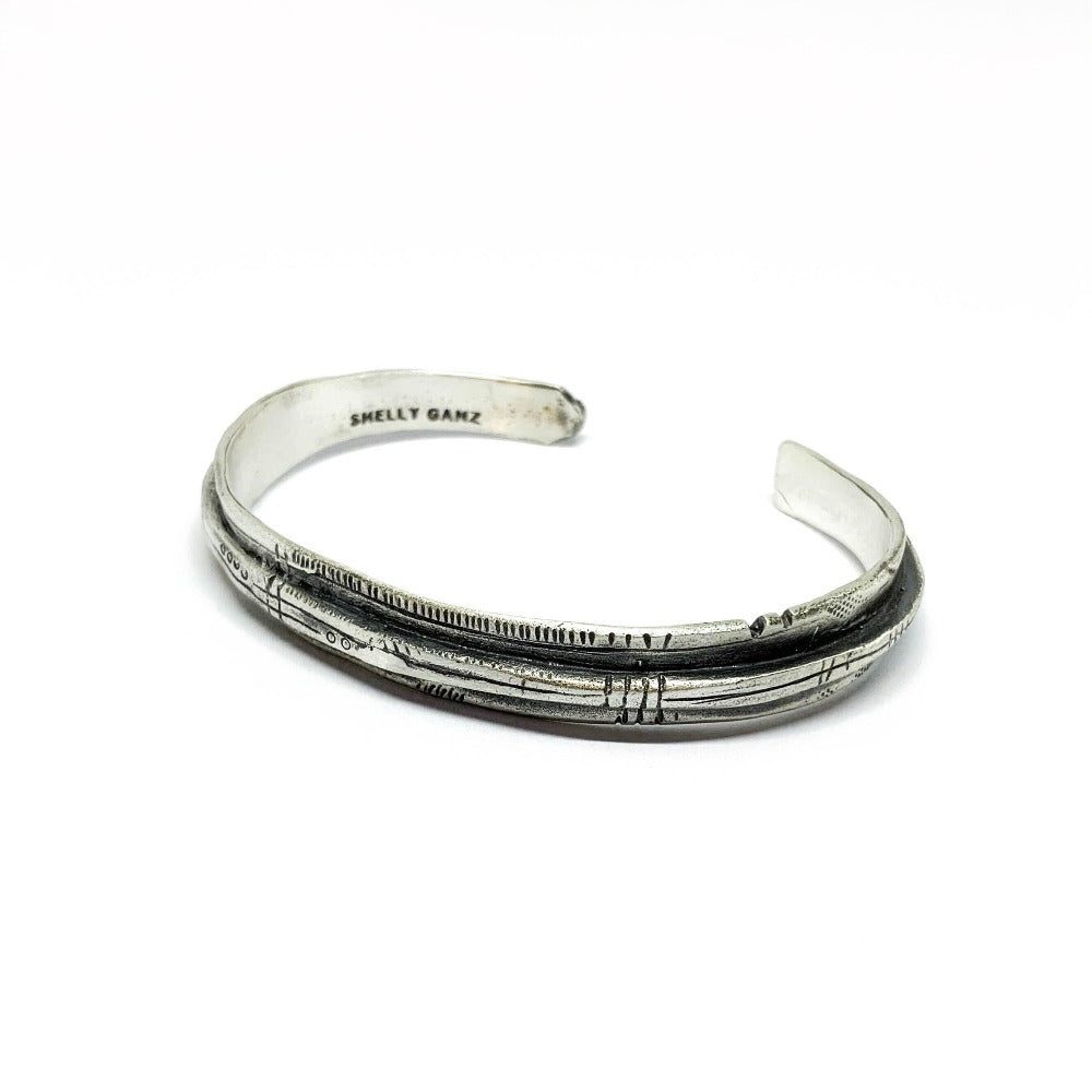 A sterling silver bracelet with an oxidized and brushed finish, featuring text on the bracelet surface.