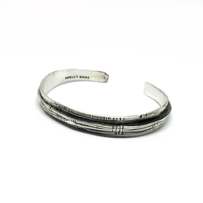 A sterling silver bracelet with an oxidized and brushed finish, featuring text on the bracelet surface.