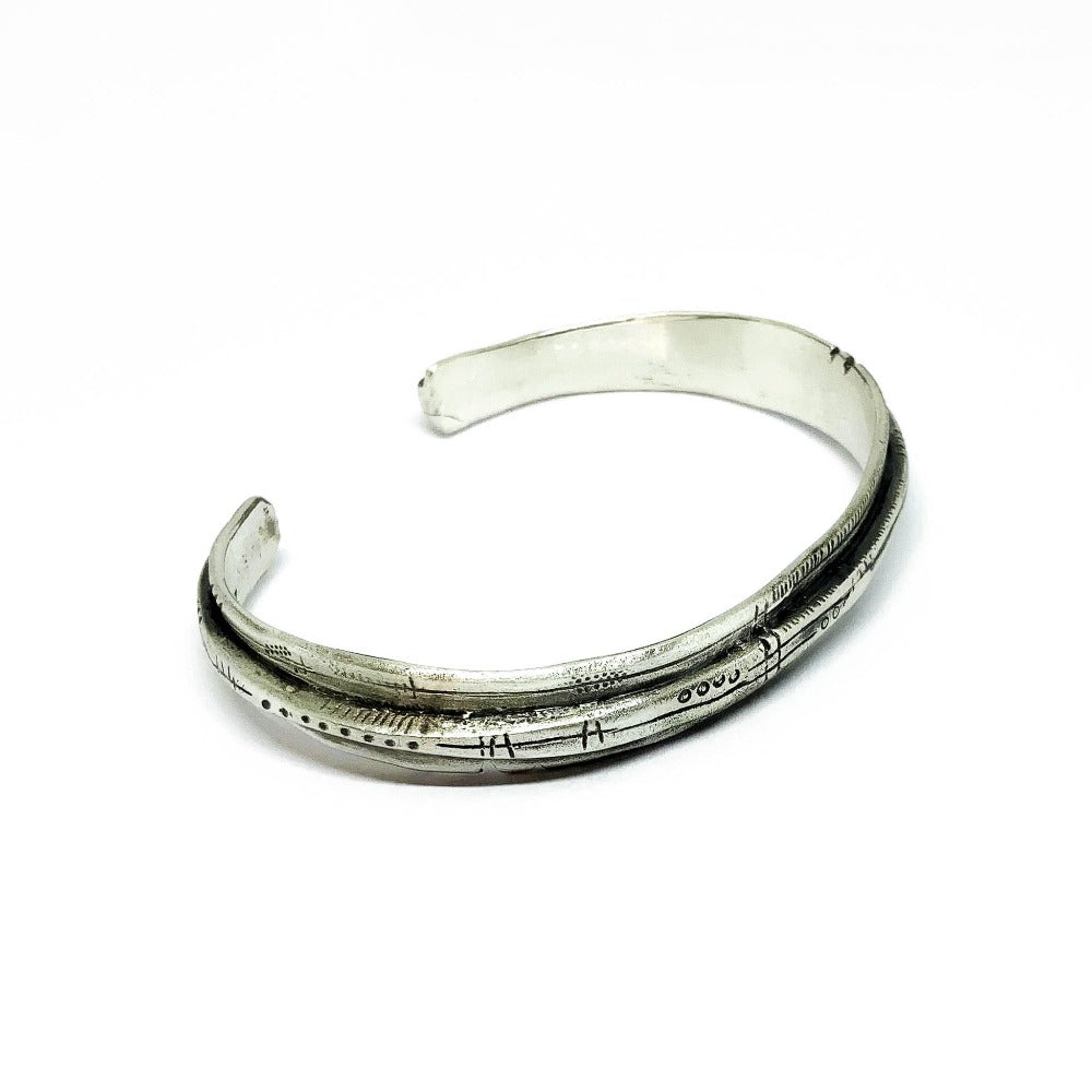 A sterling silver bracelet with an oxidized and brushed finish, featuring text on the bracelet surface.