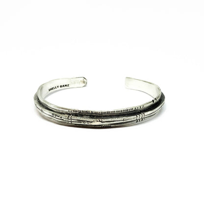 A sterling silver bracelet with an oxidized and brushed finish, featuring text on the bracelet surface.
