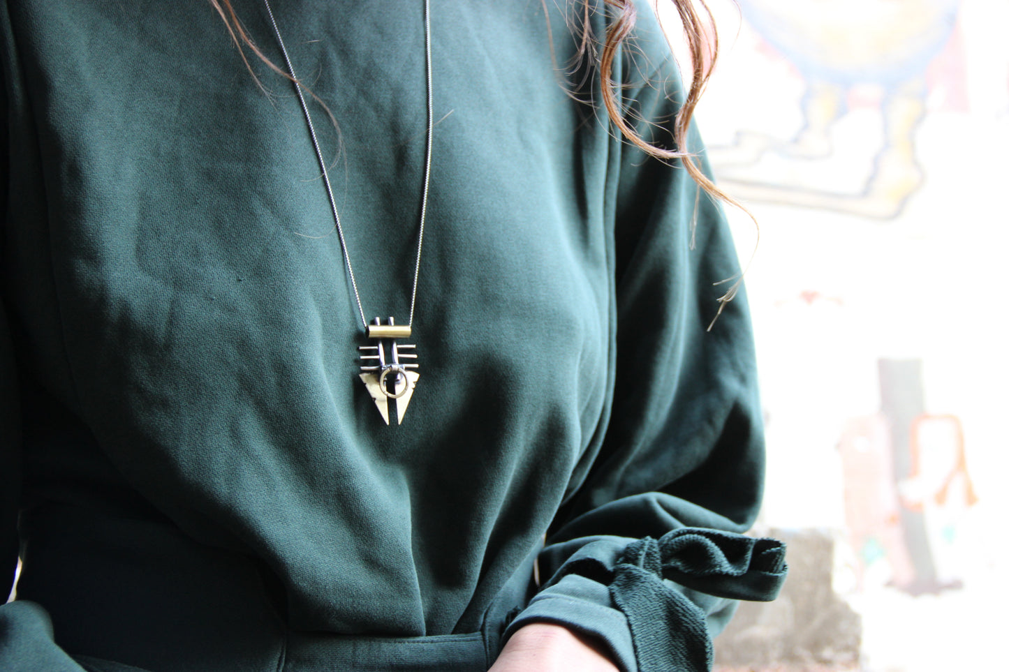 A silver and brass pendant necklace with a chain, featuring a warrior or praying mantis design.