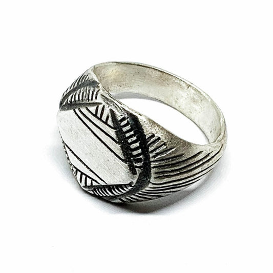 A silver signet ring with a geometric pattern on the top part, surrounded by a plain band.