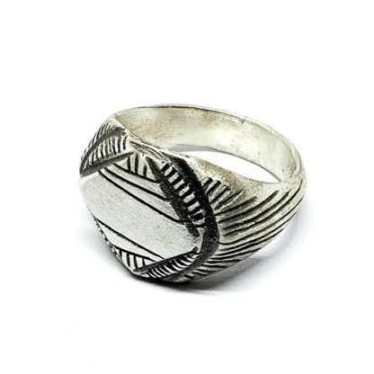 A silver signet ring with a geometric pattern on the top part, surrounded by a plain band.