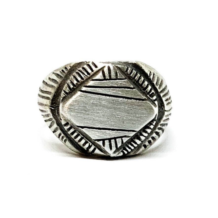 A silver signet ring with a geometric pattern on the top part, surrounded by a plain band.