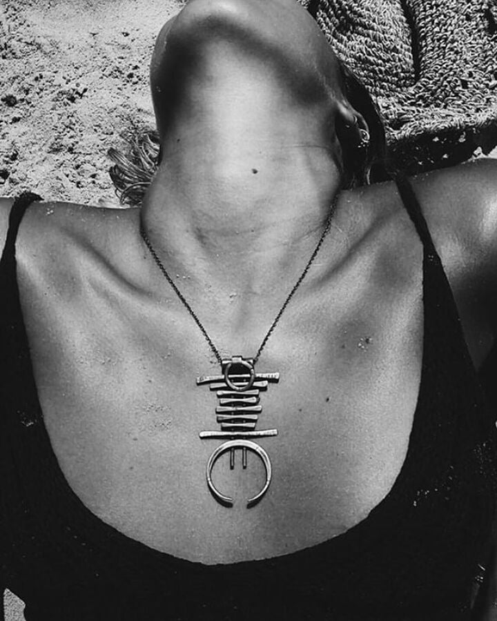 A silver and brass necklace with a geometric pendant, featuring a chain with small bell-like charms and a larger brass ring pendant.