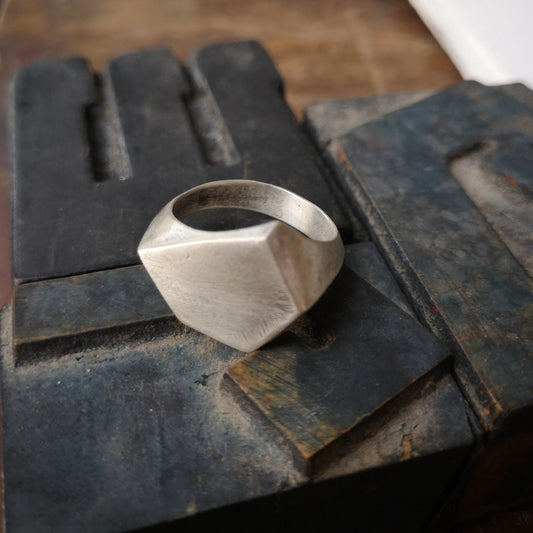 A silver ring with a geometric cutout design on the top part, with a matte finish.