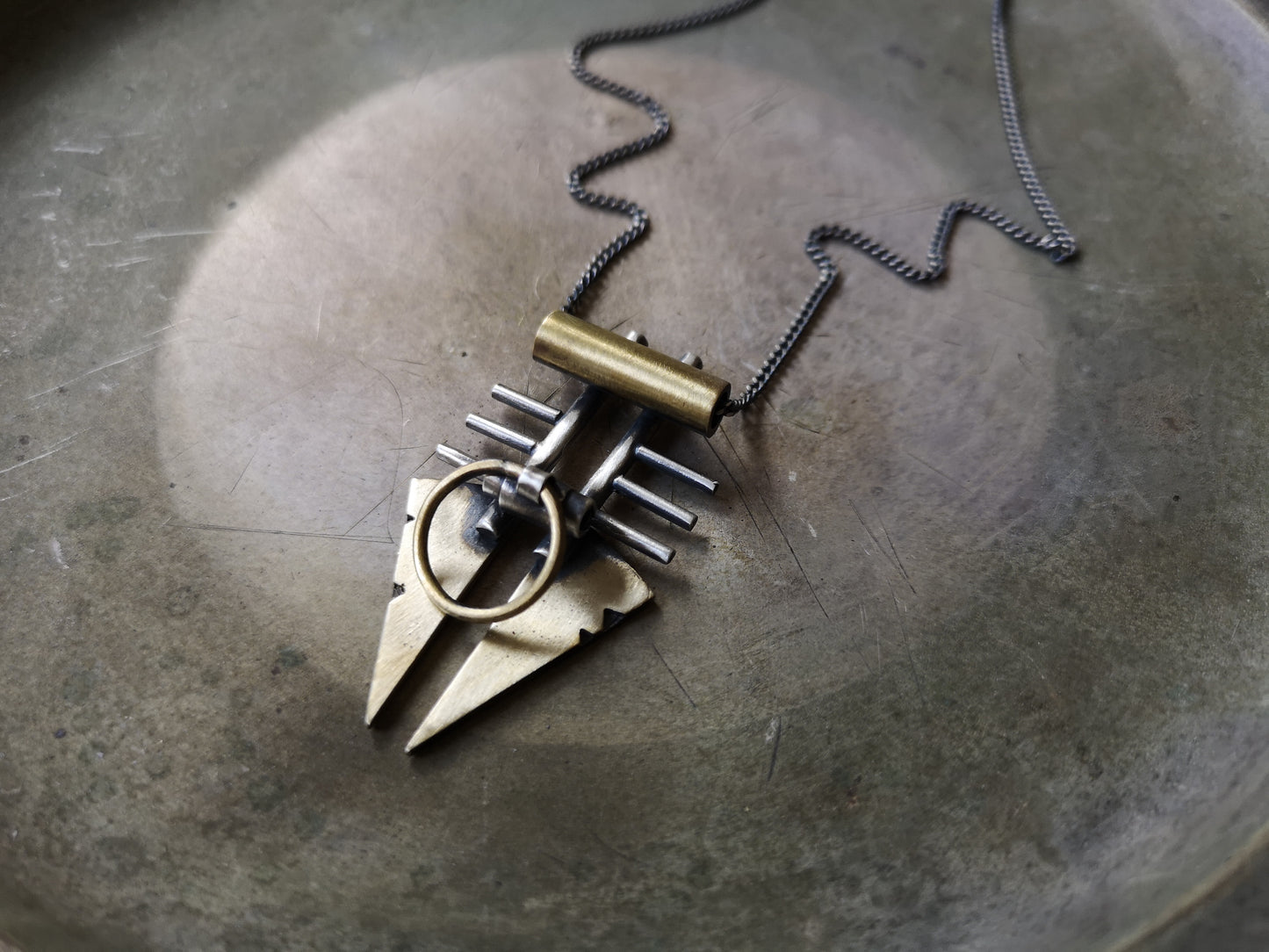 A silver and brass pendant necklace with a chain, featuring a warrior or praying mantis design.