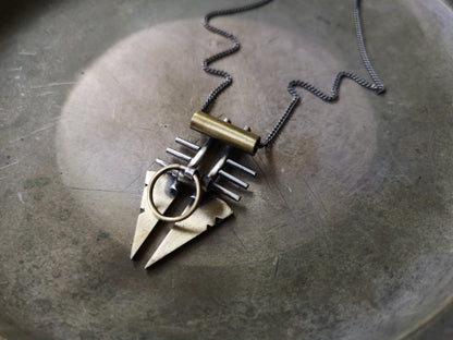 A silver and brass pendant necklace with a chain, featuring a warrior or praying mantis design.