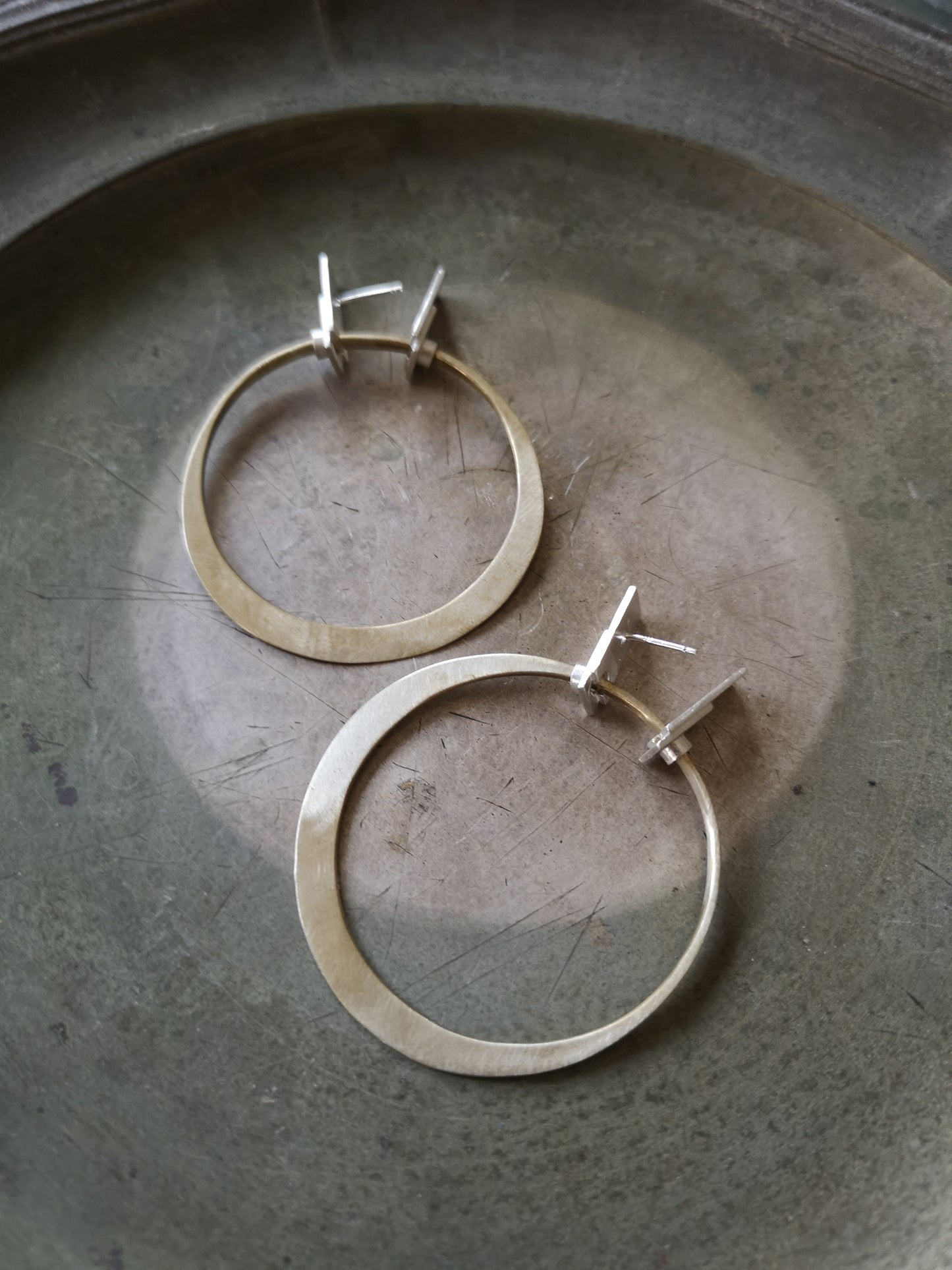 A pair of silver and brass hoop earrings with a brushed finish and a geometric design