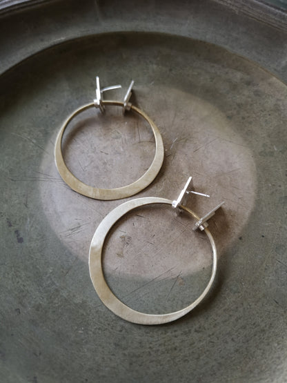 A pair of silver and brass hoop earrings with a brushed finish and a geometric design