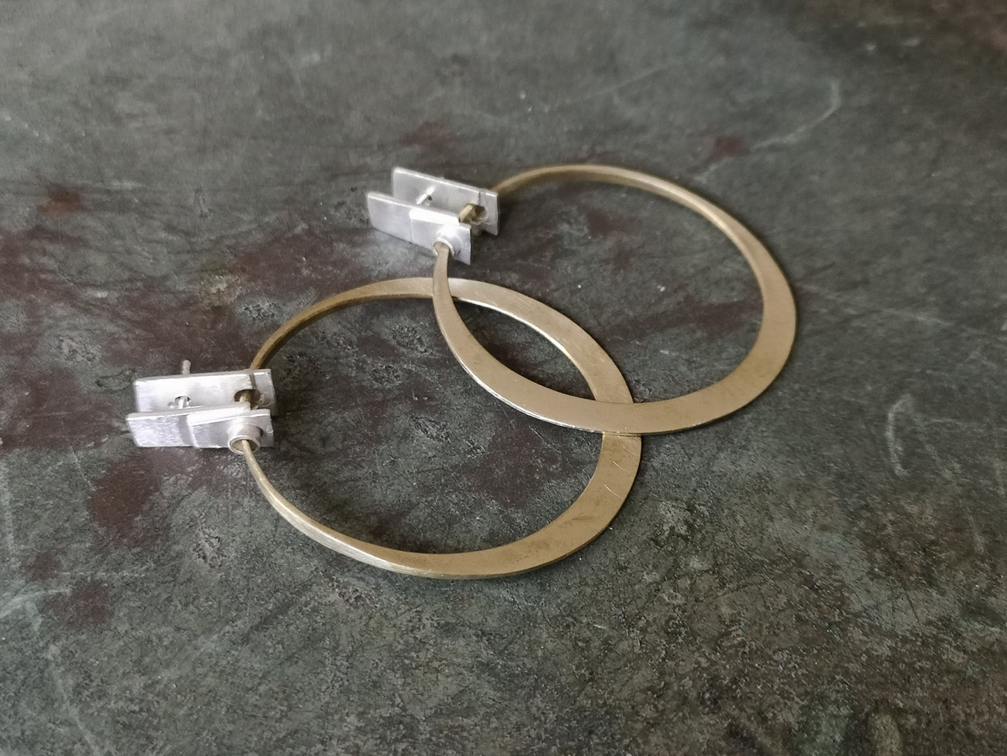 A pair of silver and brass hoop earrings with a brushed finish and a geometric design
