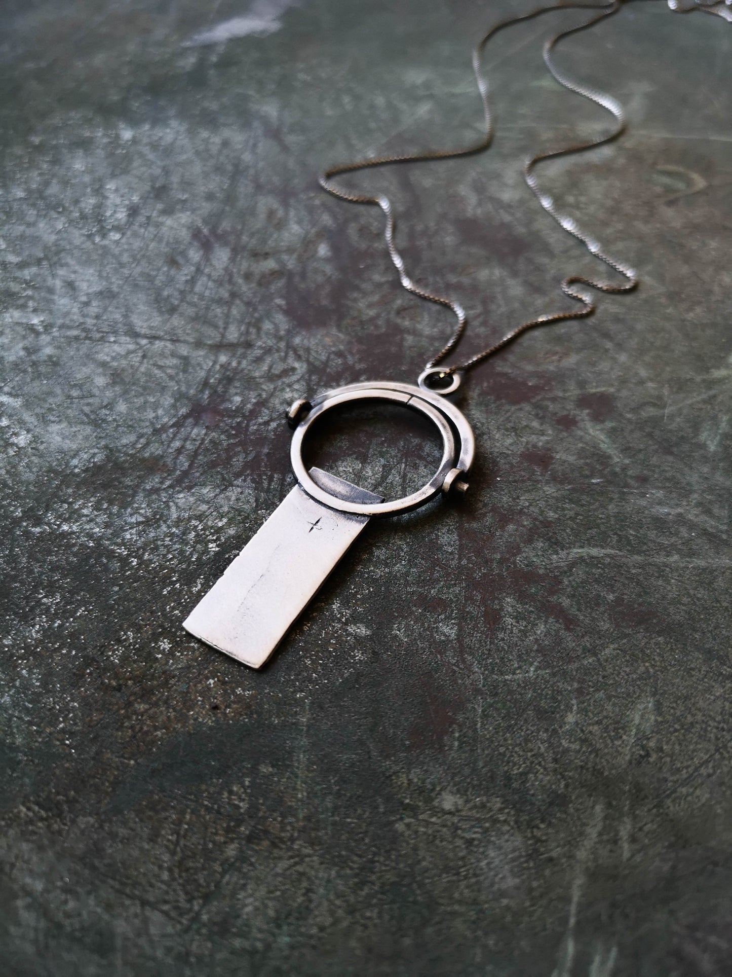 A sterling silver necklace with a magnifying glass pendant and a cross on the chain.