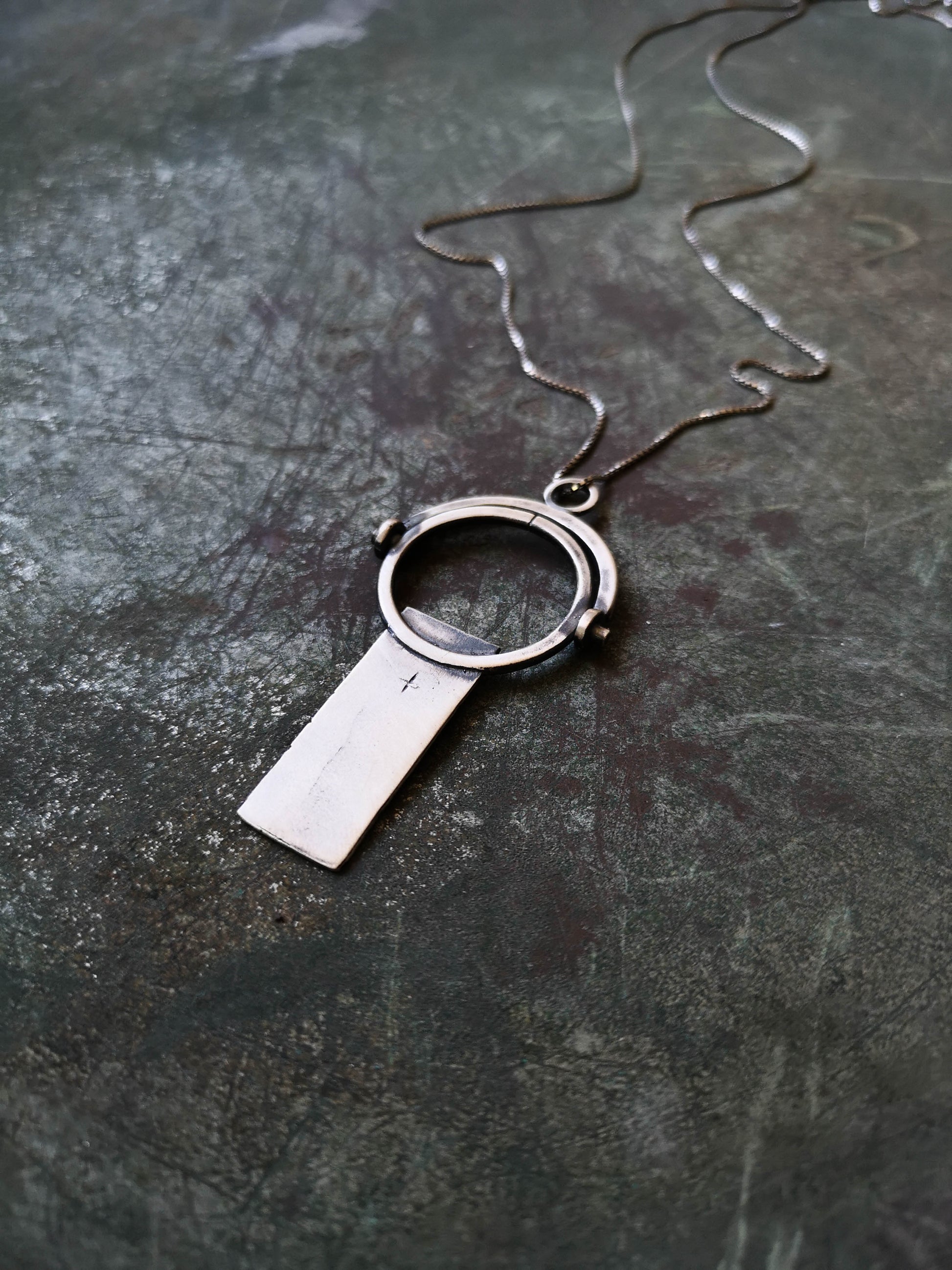 A sterling silver necklace with a magnifying glass pendant and a cross on the chain.