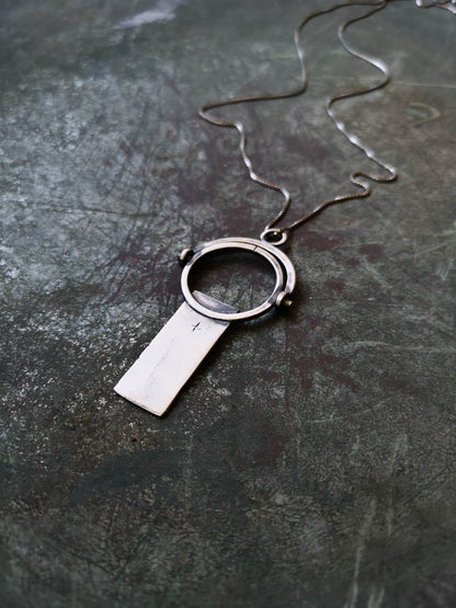A sterling silver necklace with a magnifying glass pendant and a cross on the chain.