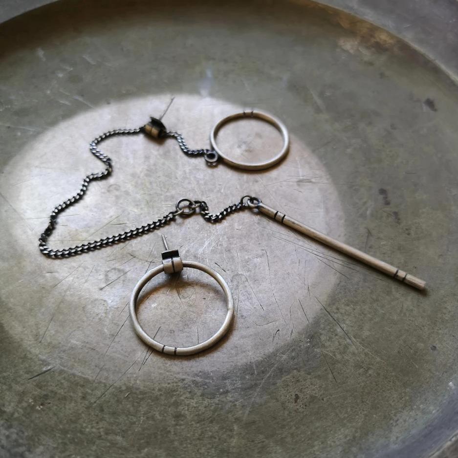 A pair of silver hoop earrings, one with a dangling tube design and the other with a chain hoop design, both made of sterling silver with a brushed finish.