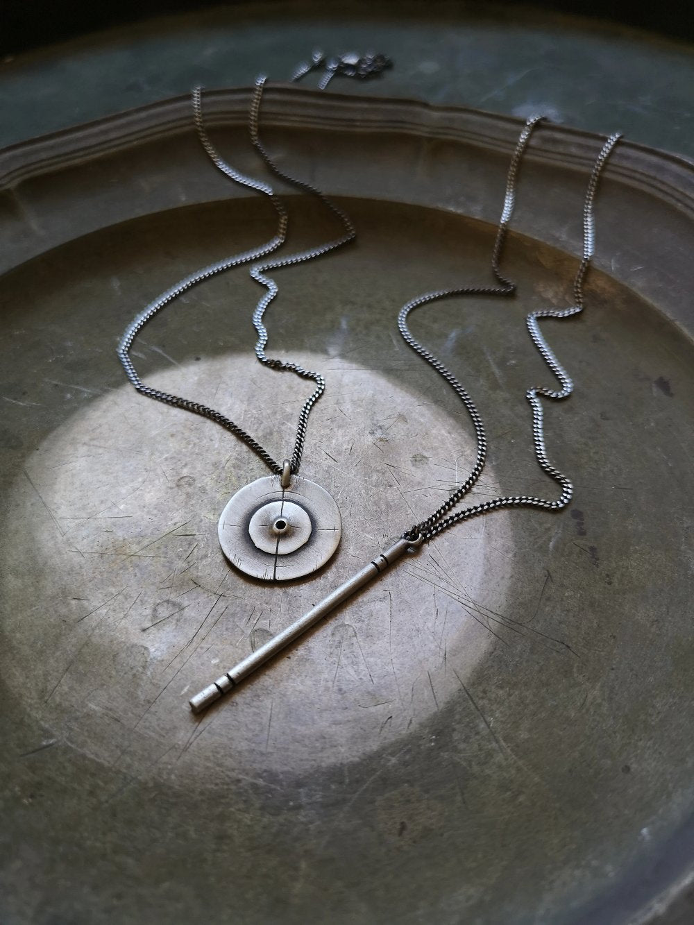 A silver necklace with a pendant resembling a stick