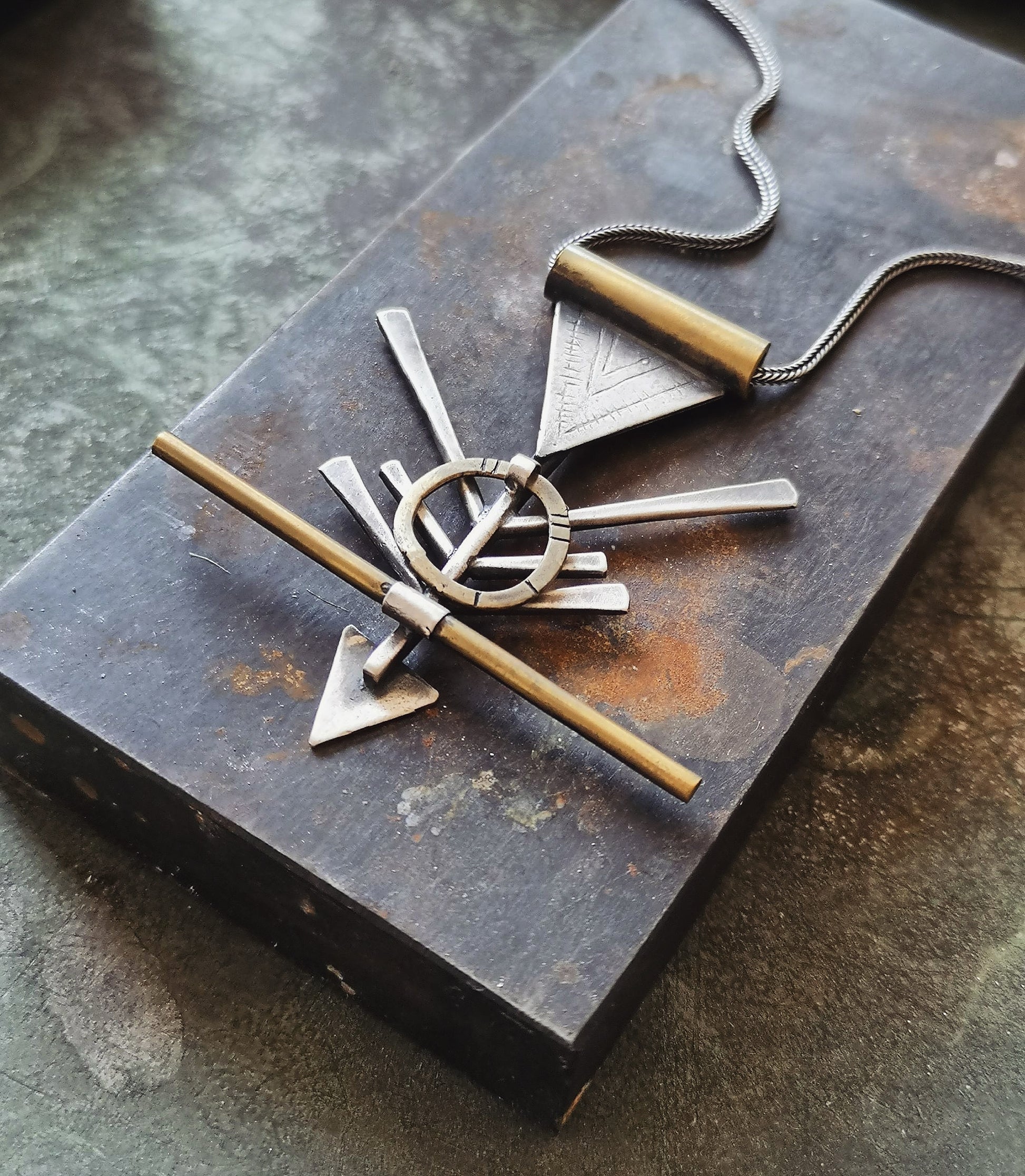 A silver and brass necklace with a geometric pendant, featuring a chain and a series of geometric shaped pendants attached to it.