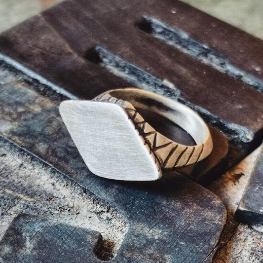 A silver ring with an oxidized and brushed finish, featuring a textured design on the top part.