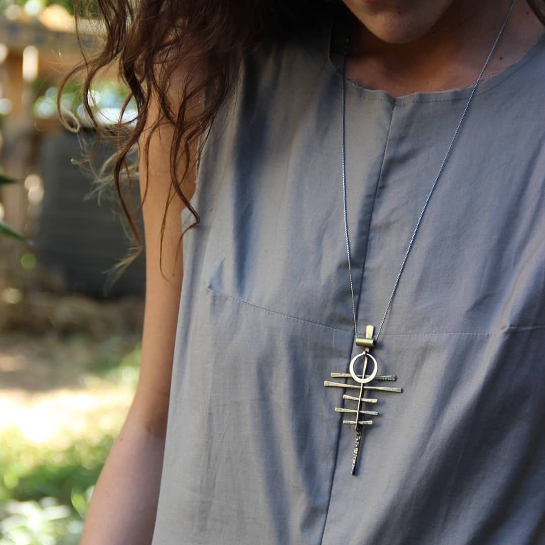 A silver-colored necklace with a pendant featuring a series of parallel lines and a circular ring