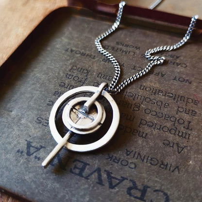 A silver necklace with a pendant featuring a circular design and a chain that ends in a pendant loop.